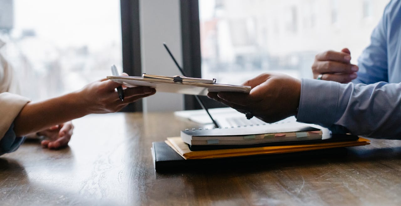 portfolio-01 Crop anonymous ethnic woman passing clipboard to office worker with laptop during job interview