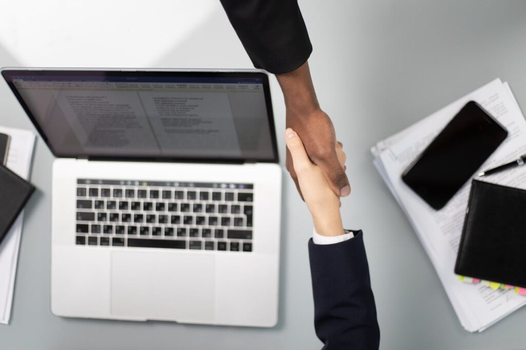 pexels-photo-6077983 Overhead view of a professional handshake over a laptop, symbolizing business agreement.
